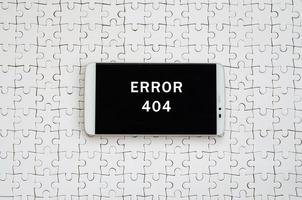 A modern big smartphone with a touch screen lies on a white jigsaw puzzle in an assembled state with inscription. Error 404 photo