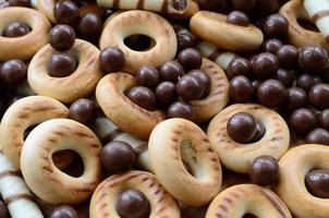 A lot of crispy sweet tubules, chocolate melting balls and yellow bagels lie on a wooden surface. Close up view photo