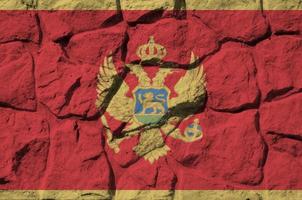 bandera de montenegro representada en colores de pintura en el primer plano de la pared de piedra antigua. banner texturizado sobre fondo de pared de roca foto