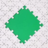 Framing in the form of a rhombus, made of a white jigsaw puzzle around the green space photo