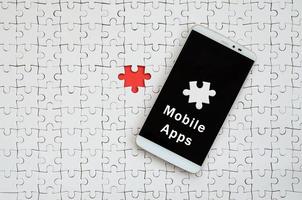 A modern big smartphone with a touch screen lies on a white jigsaw puzzle in an assembled state with inscription. Mobile apps photo