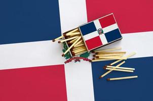 la bandera de la república dominicana se muestra en una caja de cerillas abierta, de la que caen varias cerillas y se encuentra en una gran bandera foto