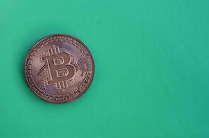 Chocolate product in the form of physical bitcoin lies on a green plastic background. Model of the crypto currency in the edible form photo