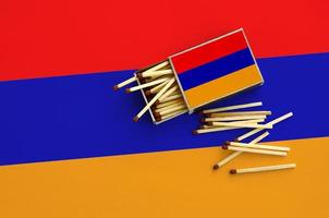 Armenia flag is shown on an open matchbox, from which several matches fall and lies on a large flag photo