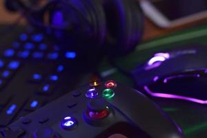 Modern gamepad and gaming mouse lies with keyboard and headphones on table in dark playroom scene. Esports and cyber sport tournament concept photo