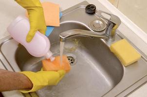 Cleaner applying liquid soap from cleanser detergent bottle to sponge at home photo