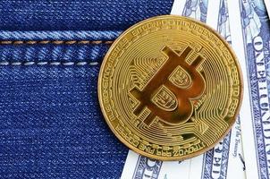 Golden Bitcoin and dollar bills lies on a blue jeans fabric. New virtual money. New crypto currency in the form of the coins photo