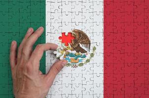 la bandera de méxico está representada en un rompecabezas, que la mano del hombre completa para doblar foto