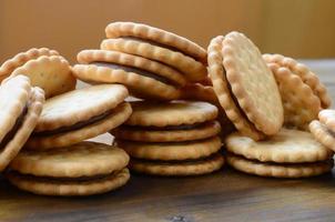 A round sandwich cookie with coconut filling lies in large quantities on a brown wooden surface. Photo of edible treats on a wooden background with copy space