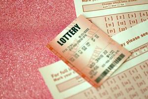 Red lottery ticket lies on pink gambling sheets with numbers for marking to play lottery. Lottery playing concept or gambling addiction. Close up photo