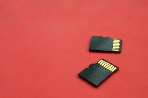 dos pequeñas tarjetas de memoria micro sd se encuentran sobre un fondo rojo. un pequeño y compacto almacén de datos e información foto