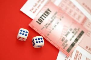 Red lottery ticket with dice lies on pink gambling sheets with numbers for marking to play lottery. Lottery playing concept or gambling addiction. Close up photo