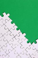 Fragment of a folded white jigsaw puzzle on the background of a green plastic surface. Texture photo with copy space for text
