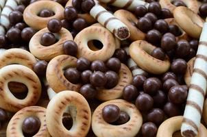 A lot of crispy sweet tubules, chocolate melting balls and yellow bagels lie on a wooden surface. Close up view photo