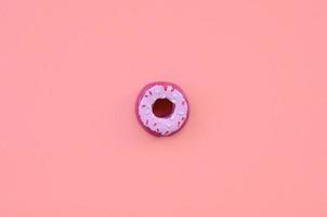 Single small plastic donut lies on a pastel colorful background. Flat lay minimal composition. Top view photo