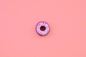 Single small plastic donut lies on a pastel colorful background. Flat lay minimal composition. Top view photo