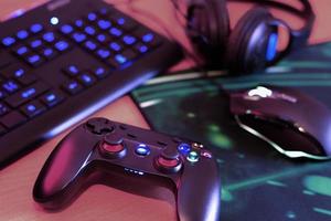 Modern gamepad and gaming mouse lies with keyboard and headphones on table in dark playroom scene. Devices for playing video games at home photo