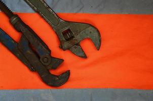 Adjustable and pipe wrenches against the background of an orange signal worker shirt photo