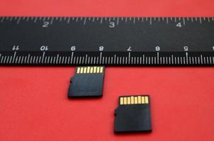 Two small micro SD memory cards lie on a red background next to a black ruler. A small and compact data and information store photo