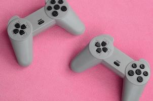 Playing games concept. Two pad joysticks lies on the blanket of furry pink fleece fabric. Controllers for video games on a background texture of light pink soft plush fleece material photo