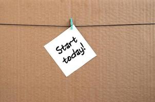 Start today Note is written on a white sticker that hangs with a clothespin on a rope on a background of brown cardboard photo