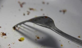 Fork on white plate with cake or brownies snack crumbs leftover. After eating diet photo on plain background.