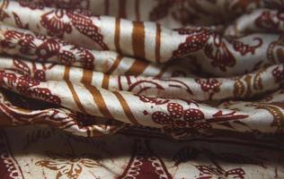 Close up textured soft drapery fabric garment or clothing with shadow folds, with brown pattern traditional on white fabric background. photo