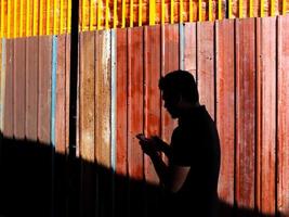 Silhouette  of a man texting on the phone against bright metal wall photo