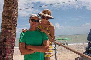 Mature couple at the beach in Combuco, Brazil, on a sunny day standing near a palm tree photo