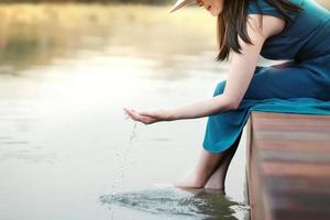 vida desconectada o vida humana con el concepto de naturaleza. joven feliz relajándose junto al río. sonriendo y sentado en la cubierta, tocando el agua con la mano foto