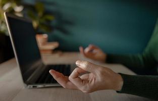 concepto de equilibrio de vida laboral. mujer sentada en el escritorio y haciendo la meditación mientras trabaja en la computadora portátil. salud mental y calma pensativa. reducir la velocidad del trabajo de estrés foto