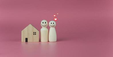 Happy house concept. Model house with wooden dolls standing lined up on pink background and heart icons. Indicates happiness and love in the home. photo