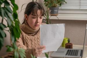 chica trabaja con documentos sentados frente a una computadora portátil en su escritorio foto