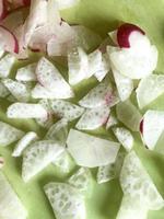 Fresh radish white and red sliced in slices on a green background. Photo daikon Top view. Vertical format