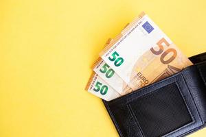 Fifty euro banknotes inside a black wallet on yellow background, cash paper currency, payment, earning and savings, european currency, money and finance concept photo