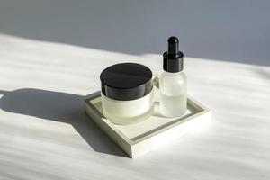 Set of skin care cosmetic products. Frosted glass jar and dropper bottle on square concrete tray with harsh shadows. Face treatment concept photo