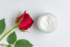 open glass jar with face xream next to red blooming rose. Skin care anti age. Anti wrinkle cosmetics. Top view with copy space photo
