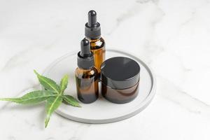 Cannabis face cream and serum or oil dropper concept. Natural cosmetic. CBD oil, THC tincture and hemp leaves on a marble table background photo