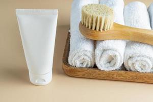 SPA cosmetics, woman body and skincare products on wooden tray on beige background. Natural bristle dry massage brush and body or face cream in white plastic tube. photo