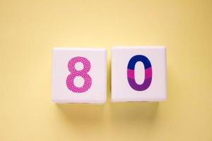 Close-up photo of a white plastic cubes with a colorful number 80 on a yellow background. Object in the center of the photo