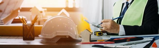 Two colleagues discussing data working and tablet, laptop with on on architectural project at construction site at desk in office photo