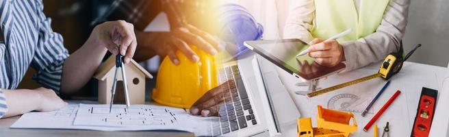 Two colleagues discussing data working and tablet, laptop with on on architectural project at construction site at desk in office photo