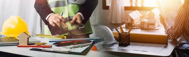 Two colleagues discussing data working and tablet, laptop with on on architectural project at construction site at desk in office photo