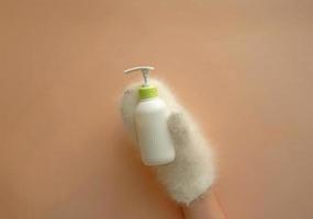 Cosmetic pump bottle of moisturizing lotion hold hands in mittens on pastel background. White corrugated bottle surface soap dispenser pump. Hand skin care lotion in winter. photo