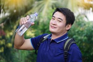 Handsome Asian man traveler holds bottle of drinking water to drink outdoors. Concept, Drinking water for health, Healthy lifestyle.Quenching thirst,reduce fatigue, refreshes body. photo