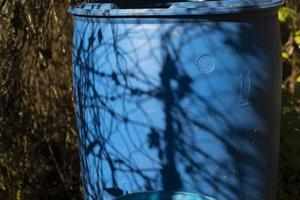 Blue water barrel in garden. Blue barrel and shade from plants. Plastic container. photo