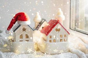 Cozy house is wrapped in a hat and scarf in a snowstorm -window sill decor. Winter, snow - home insulation, protection from cold and bad weather, room heating system. Festive mood, Christmas, New Year photo