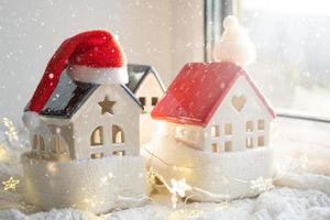 Cozy house is wrapped in a hat and scarf in a snowstorm -window sill decor. Winter, snow - home insulation, protection from cold and bad weather, room heating system. Festive mood, Christmas, New Year photo