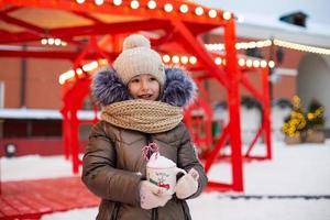 Mom and daughter for Christmas outdoor in warm clothes in winter at festive market. Fairy lights garlands decorated snow town for new year photo