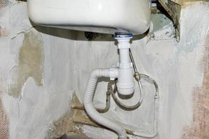 An old iron kitchen sink with a faucet in the old kitchen. Renovation in the kitchen and fresh plaster. Sink with a sanitary siphon. photo